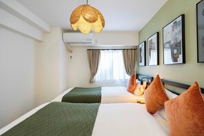 Ein Hotelzimmer mit zwei Betten, einer Hängelampe, Klimaanlage, Vorhängen und gerahmten Kunstwerken an der Wand.