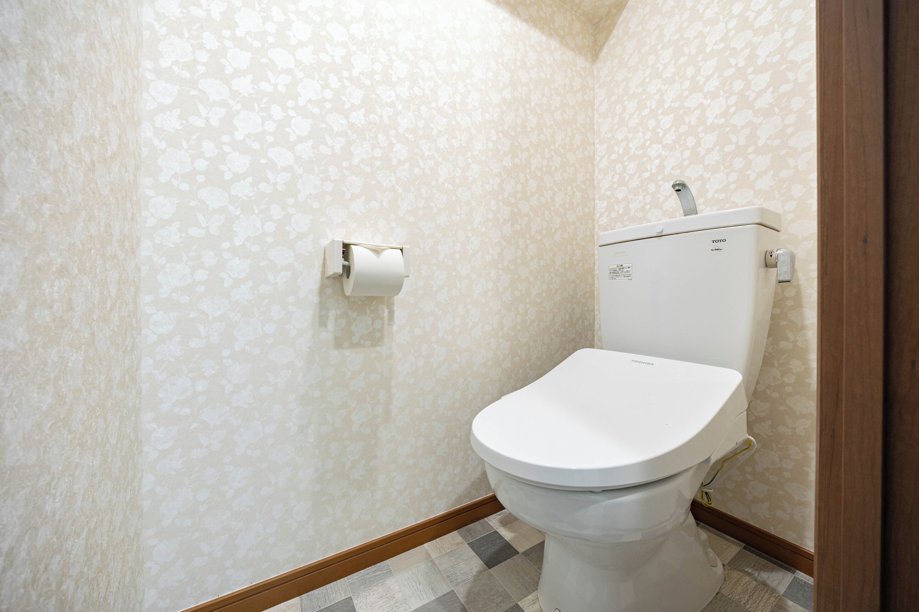 A bathroom with a toilet, a toilet paper holder, and patterned wallpaper.