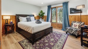 Ein Schlafzimmer mit einem Bett, Nachttischen, einem Sessel, einer Lampe und einem Fenster mit Vorhängen.