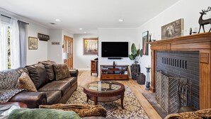 Ein Wohnzimmer mit Ledersofa, Glastisch, Kamin und Wand-Fernseher.