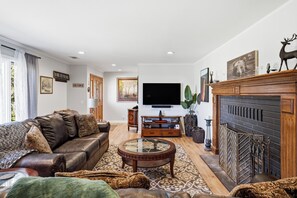A living room with a leather sofa, a glass coffee table, a fireplace, and a television mounted on the wall. - Wildflower Ridge, Near Yosemite & Bass Lake (Oakhurst)