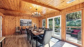 Ein Holzinterieur mit einem für sechs Personen gedeckten Esstisch, einer Kristallleuchter und großen Fenstern mit Blick ins Freie.