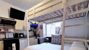 A bunk bed with a TV above it, a kitchen area, and a window with a view. - Entire London center studio flat Victorian build/quiet/mins tube river/1 shower (London)