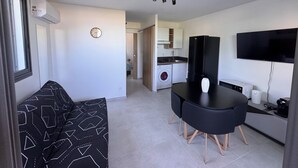 A compact living space with a kitchenette, a dining area with a black table and chairs, a sofa with a geometric pattern, a mounted TV, and a washing machine. - T2 any comfort Tranquillity assured has only 5 min of st stone (Saint-Pierre)