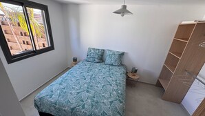 A bedroom with a bed, a window, a bedside table, a lamp, and a wardrobe. - T2 any comfort Tranquillity assured has only 5 min of st stone (Saint-Pierre)