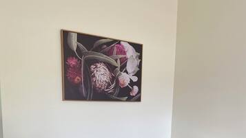 Two beige armchairs, a small white table with two mugs, and a floral painting on the wall.