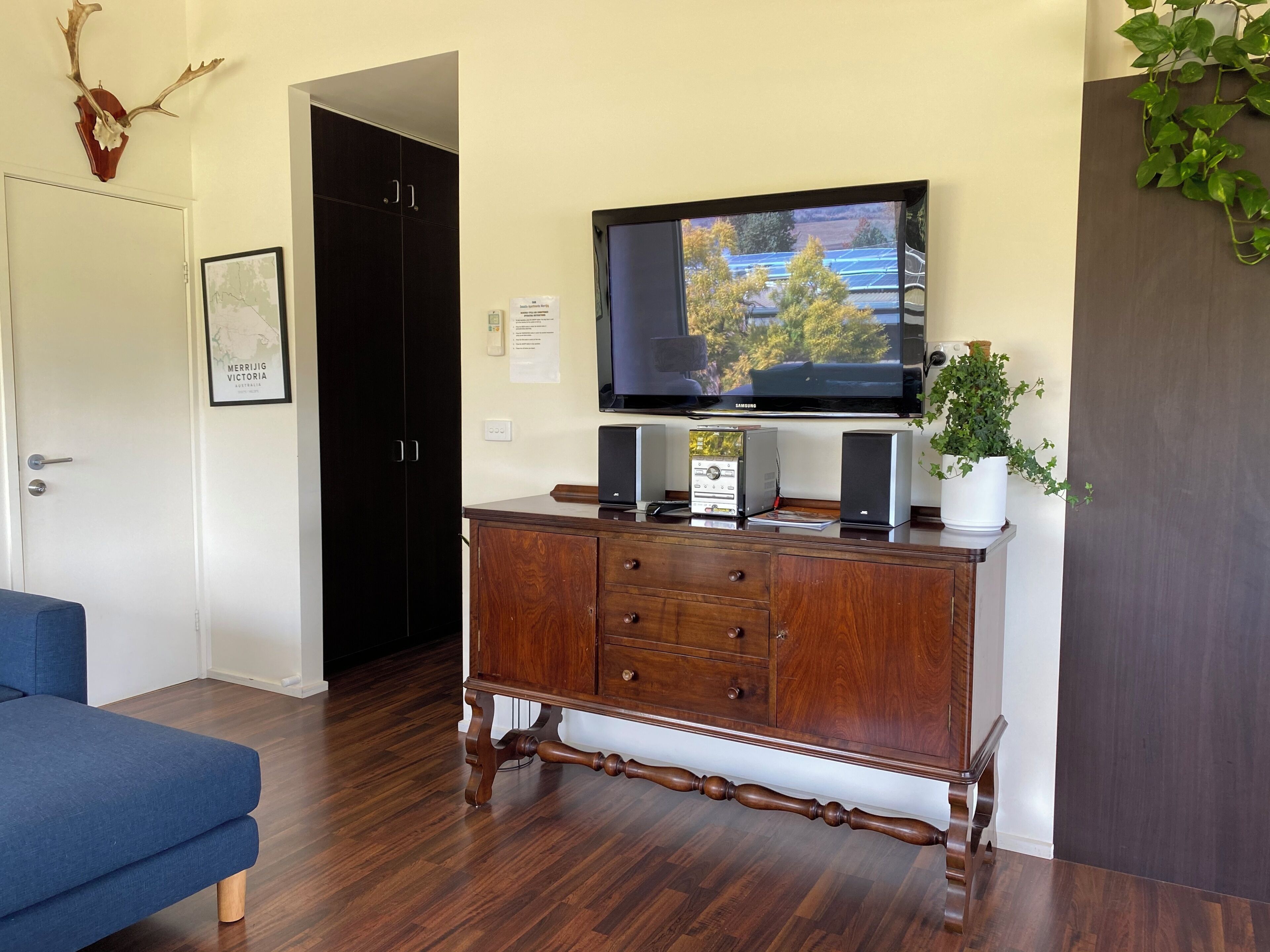 A room with a television on a wooden cabinet, a blue sofa, and a door with a framed map.