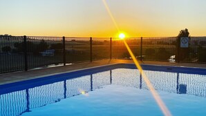 Ein Swimmingpool mit Zaun und einem Verbotsschild für Sprünge, eingebettet in eine Landschaft bei Sonnenuntergang.