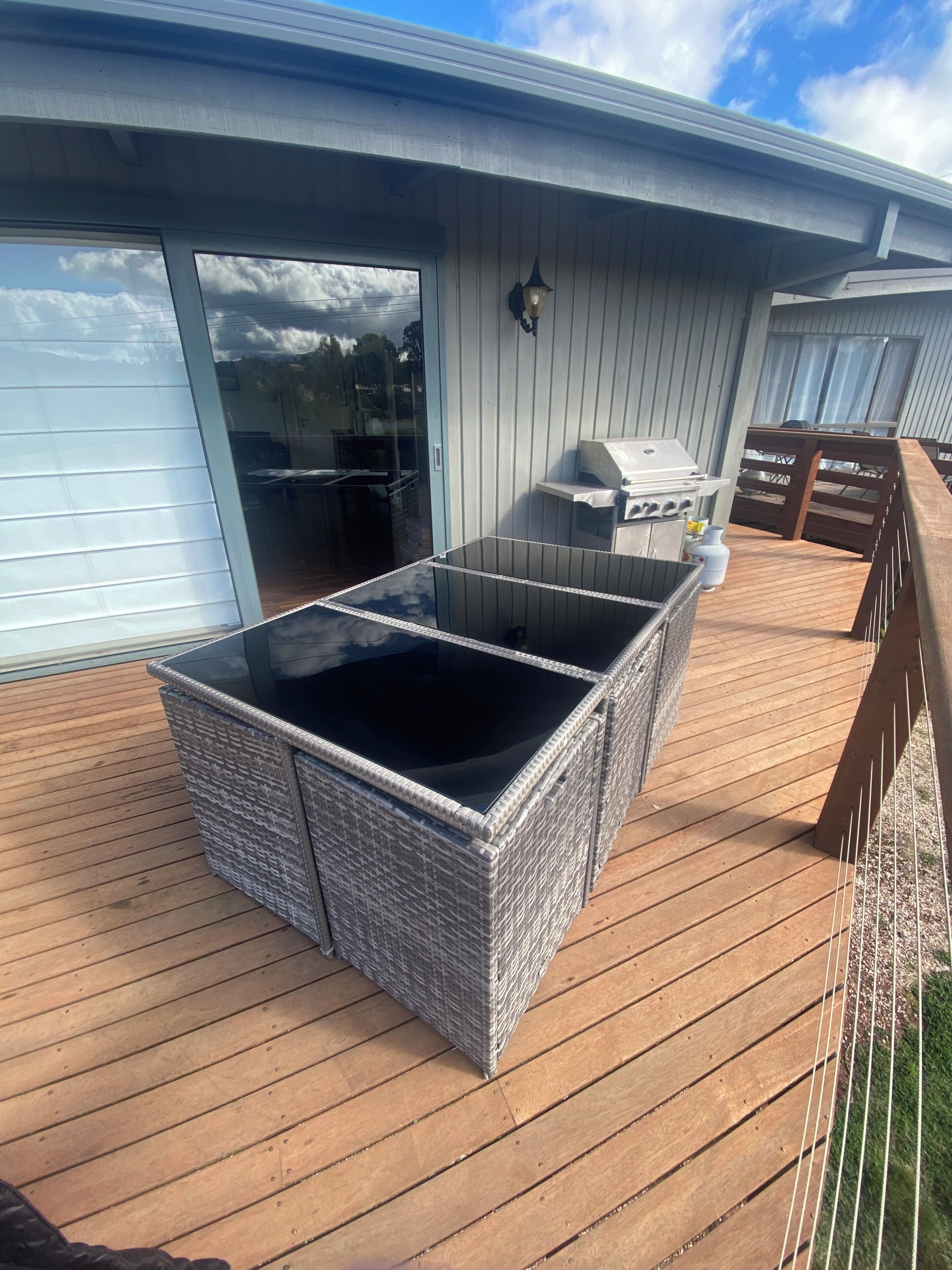 A wicker outdoor seating area with a glass top, a barbecue grill, and a wooden deck.