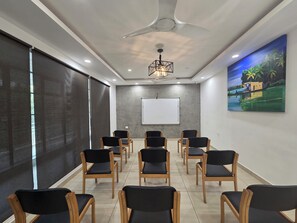 Une salle de conférence équipée d’un tableau blanc, d’un écran de projection, d’un ventilateur de plafond et ornée d’un tableau représentant un paysage tropical.