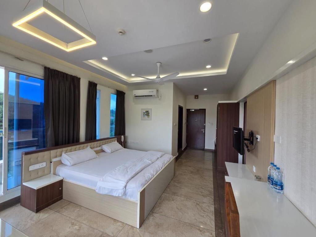 A modern hotel room with a large bed, a desk, a ceiling fan, and a view of the outdoors.