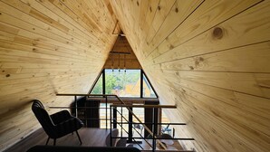 Un intérieur en bois avec un plafond en pente, une chaise et une vue par une fenêtre.