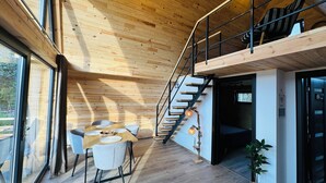 Un intérieur moderne avec un plafond en bois, un escalier, un coin repas comprenant des chaises et une table, et une vue dégagée grâce à de grandes fenêtres.