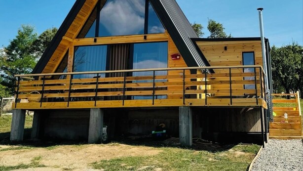 Une cabane moderne en bois, dotée d’un toit triangulaire, de grandes fenêtres et d’une terrasse en bois.