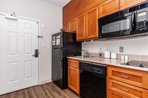 A kitchen with wooden cabinets, a black refrigerator, a microwave, a dishwasher, and a white door. - Luxury Cozy 1 bedroom Apartment with kitchenennet and full bathroom (Houston)