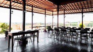An outdoor dining area with tables and chairs, large windows, and a view of the cityscape. - Nusa Dua Moon Hotel (Nusa Dua)