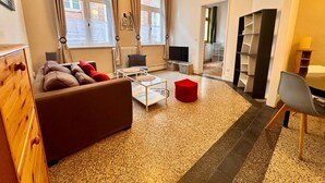 Una sala de estar moderna con un sofá, una mesa de centro y un televisor, ventanas amplias y una estantería.