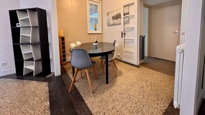 Un comedor con una mesa redonda, sillas, un estante negro y una puerta que da a otra habitación.