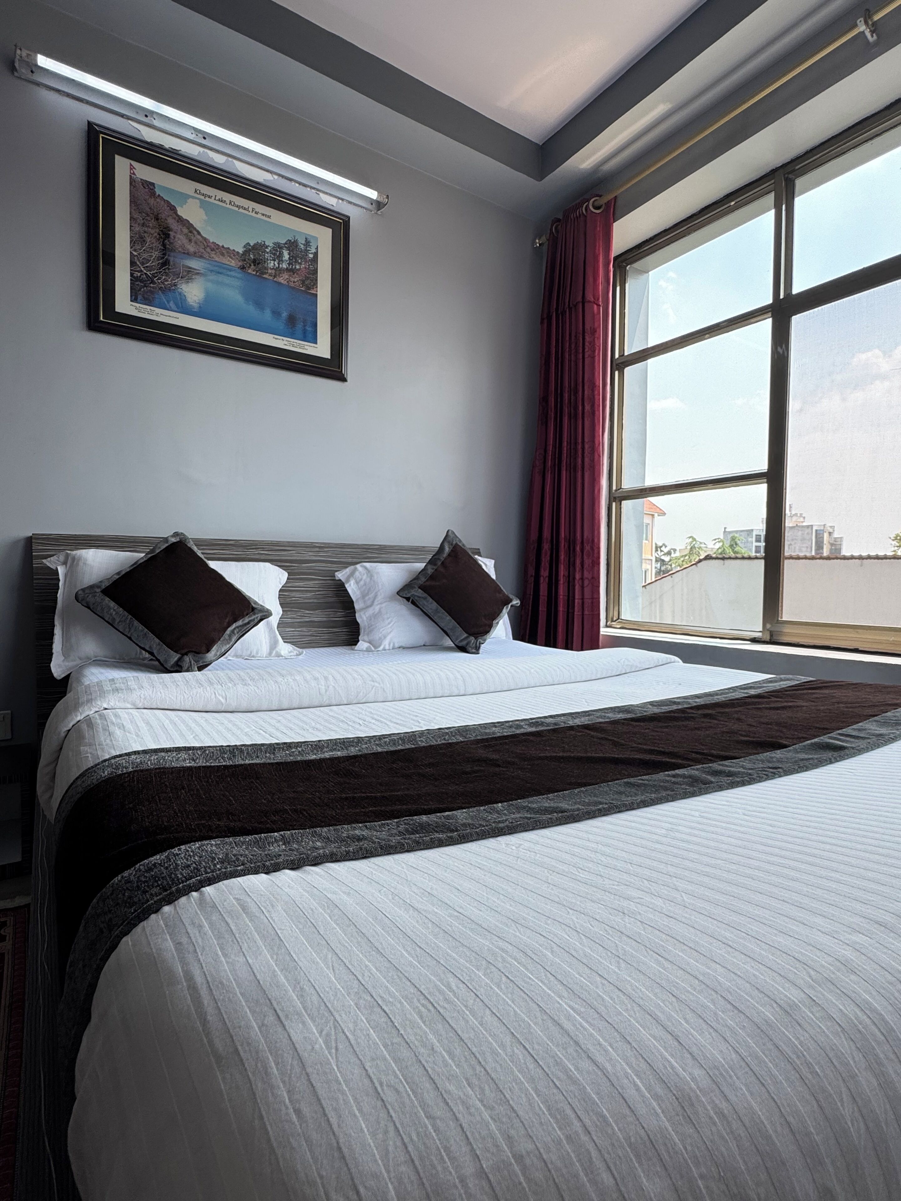 A hotel room with a large bed, a framed picture on the wall, and a window with curtains.