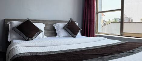 A hotel room with a large bed, a framed picture on the wall, and a window with curtains.