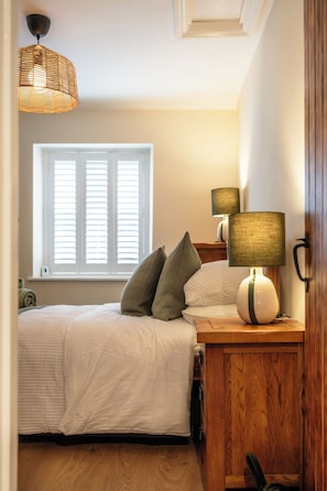 A bedroom with a bed, two bedside lamps, a window with blinds, and a wooden nightstand.