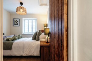 Un dormitorio con cama, lámpara de noche, ventana y lámpara colgante.