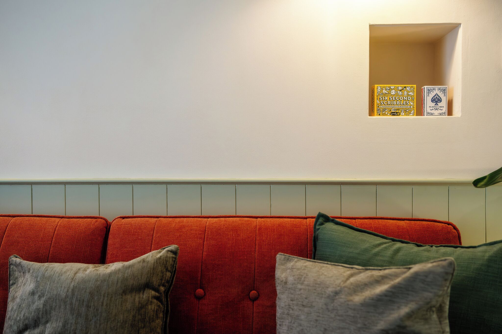 Un sofá rojo con varios cojines, una pared blanca y un estante pequeño con dos libros.