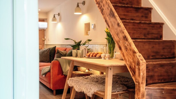 Uma área de estar aconchegante com uma escada de madeira, uma mesa de jantar com um vaso de flores e um sofá vermelho.