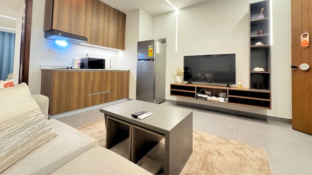 A modern living room with a sofa, coffee table, TV, kitchen area, and built-in shelves.