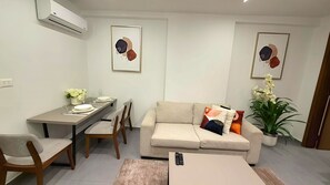 A living room with a sofa, a dining table with chairs, a potted plant, and two framed artworks on the wall.