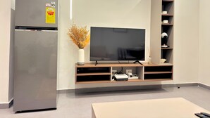 A modern living room with a flat-screen TV, a built-in wooden entertainment unit, a refrigerator, and a minimalist design.