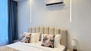 A modern hotel room with a bed, air conditioning unit, bedside lamp, and a window with curtains.