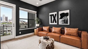 A modern living room with a leather sofa, a round ottoman, and two framed artworks on the wall.
