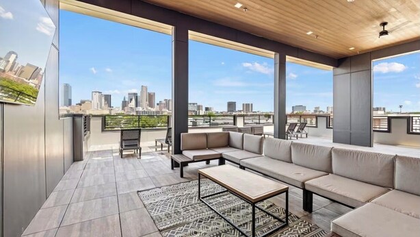 A rooftop terrace with a city skyline view, a sofa set, a coffee table, and a patterned rug.