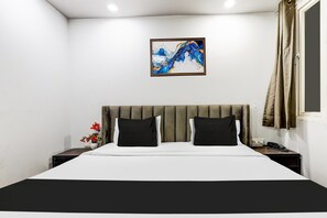A hotel room with a bed, a nightstand with a phone, a vase with flowers, and a painting on the wall.