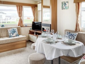 A cozy room with a sofa, a dining table set for four, a television, and a window with curtains. - The Little Sea Horse (Dornoch)
