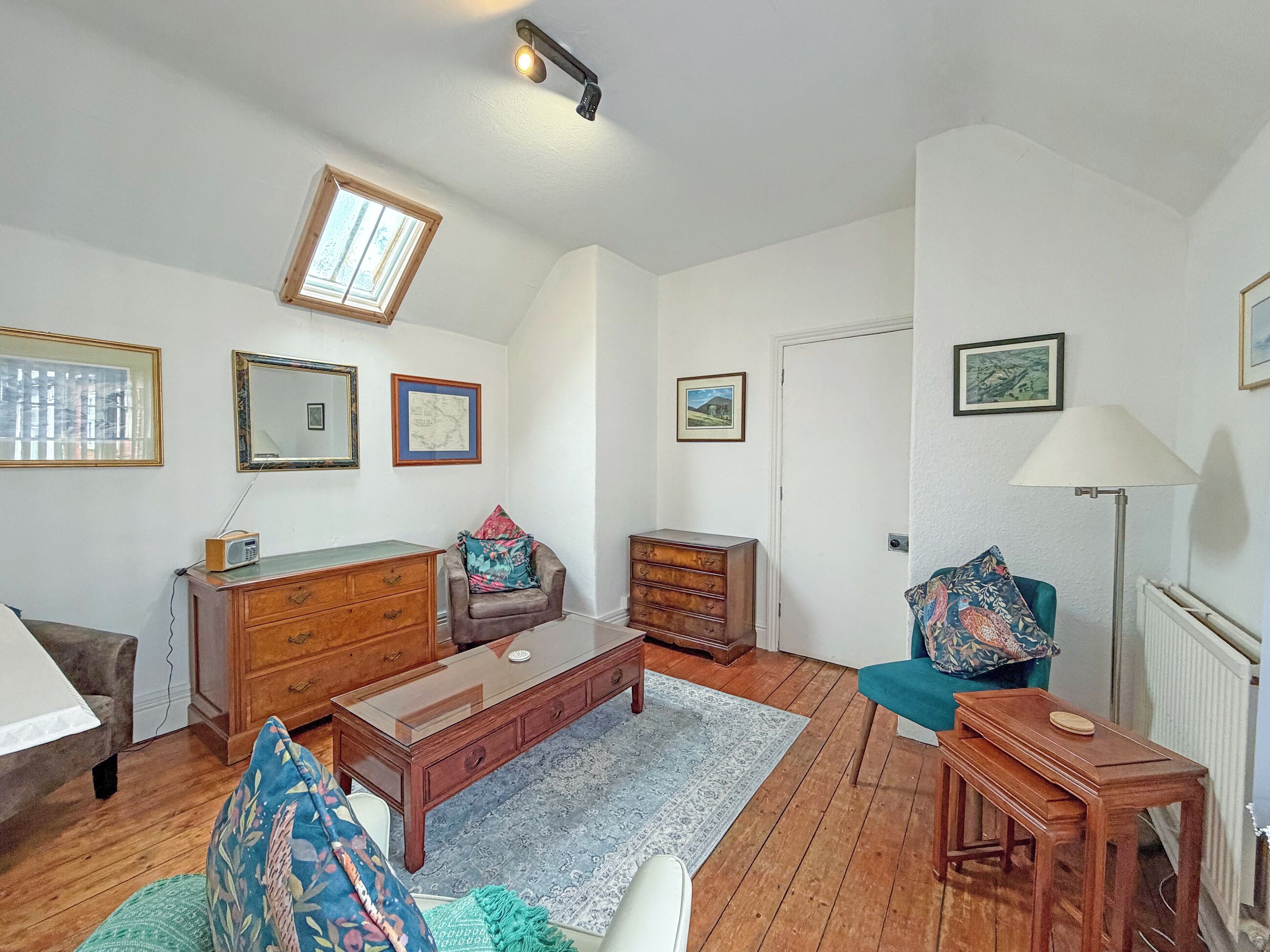 Un salon avec un plancher en bois, un canapé, une table basse, un téléviseur, une lampe et une fenêtre.