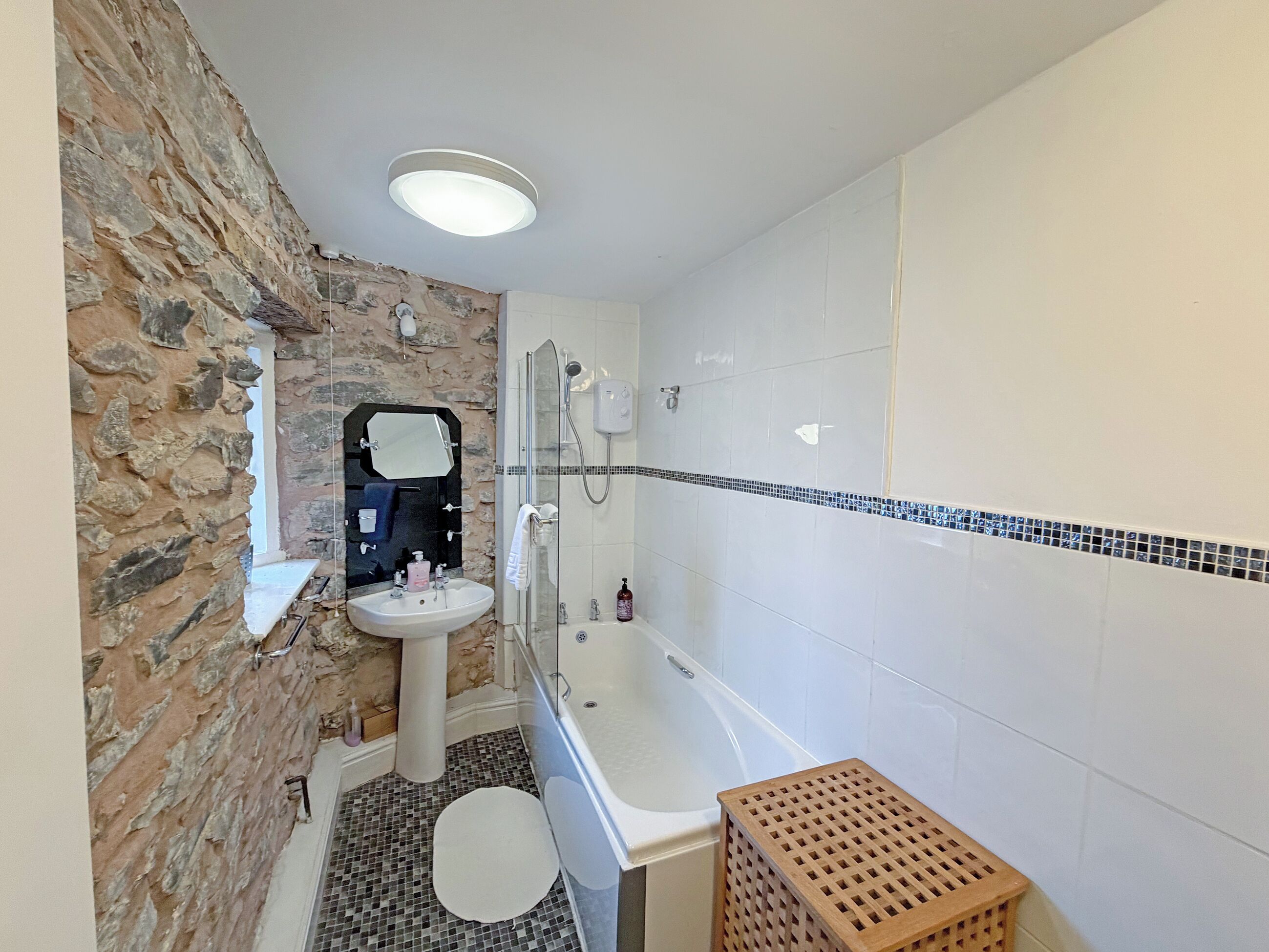 A bathroom with a stone wall, a sink, a mirror, a shower, and a tiled floor.