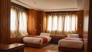 A room with wooden walls, two beds, a small table, and a window with curtains. - Samyae Resort (Jakar)