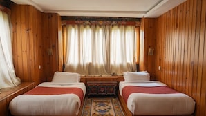 A room with two beds, wooden walls, a decorative rug, and a window with curtains. - Samyae Resort (Jakar)