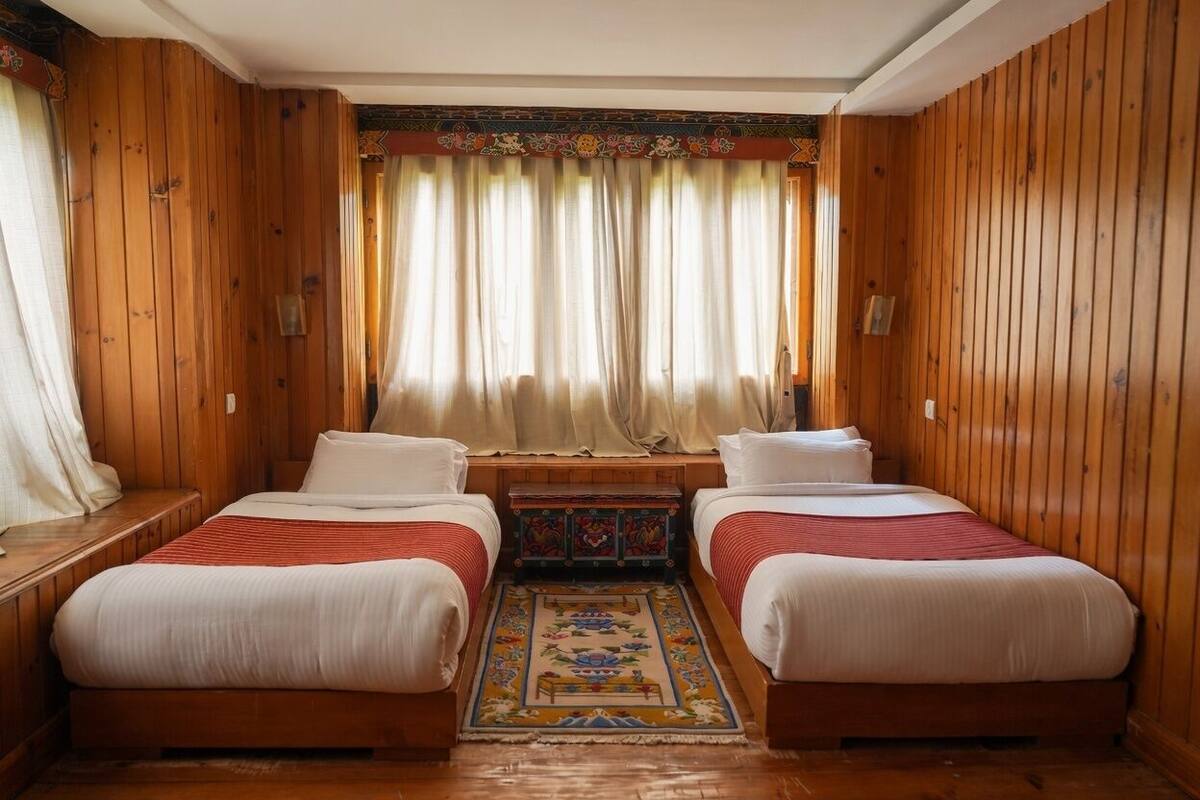 Une chambre avec deux lits, des murs en bois, un tapis décoratif et une fenêtre avec des rideaux.