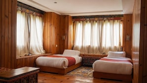 A wooden-paneled room with two beds, a small table, and a window with curtains. - Samyae Resort (Jakar)