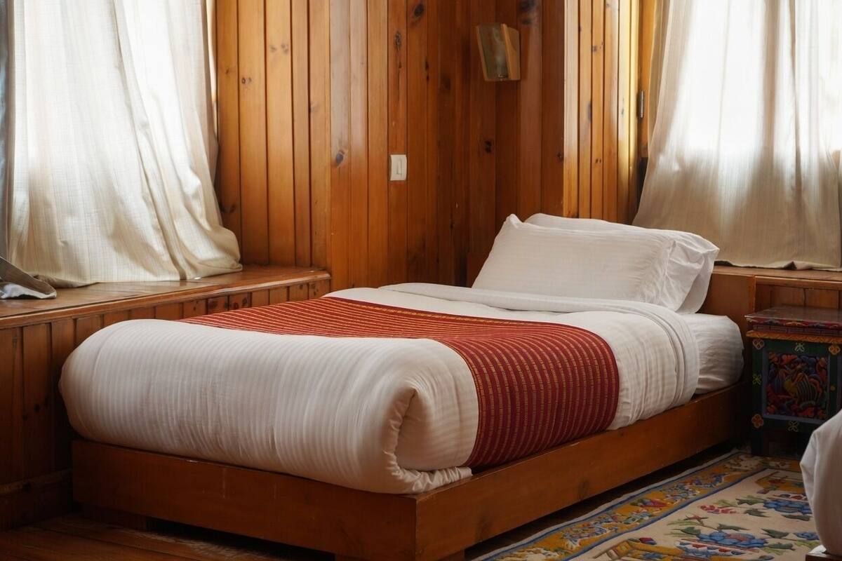 Un lit en bois avec une literie blanche et rouge, une petite table de chevet et un tapis coloré.