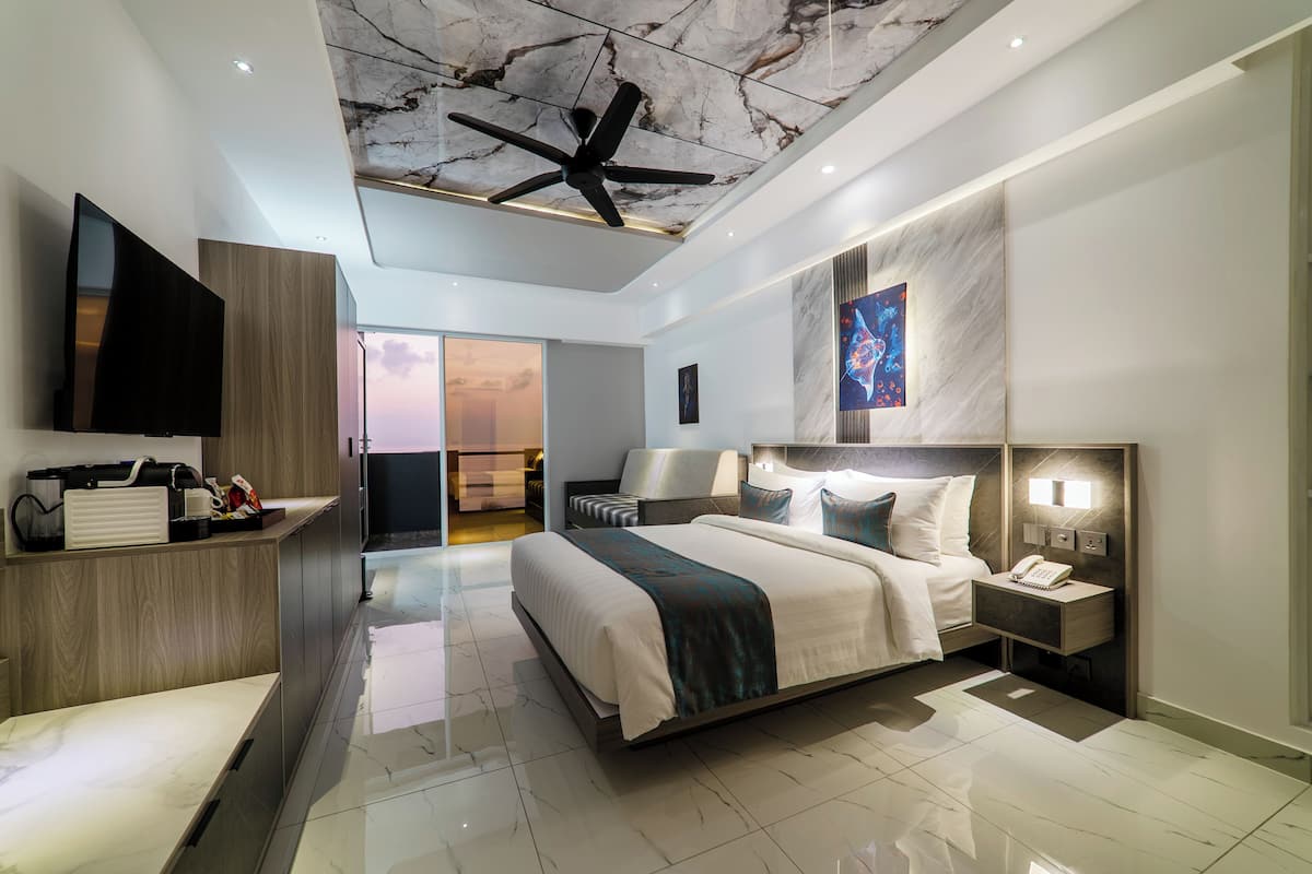 A modern hotel room with a large bed, a flat-screen TV, a desk, and a ceiling fan.
