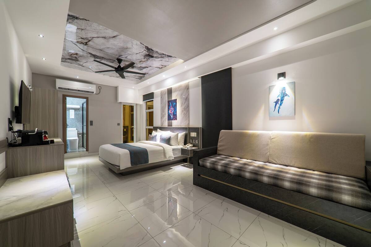 A modern hotel room with a bed, sofa, and a ceiling fan.