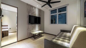 A modern living room with a sofa, a table, a ceiling fan, and a TV mounted on the wall. - Samann Blue (Hulhumale)