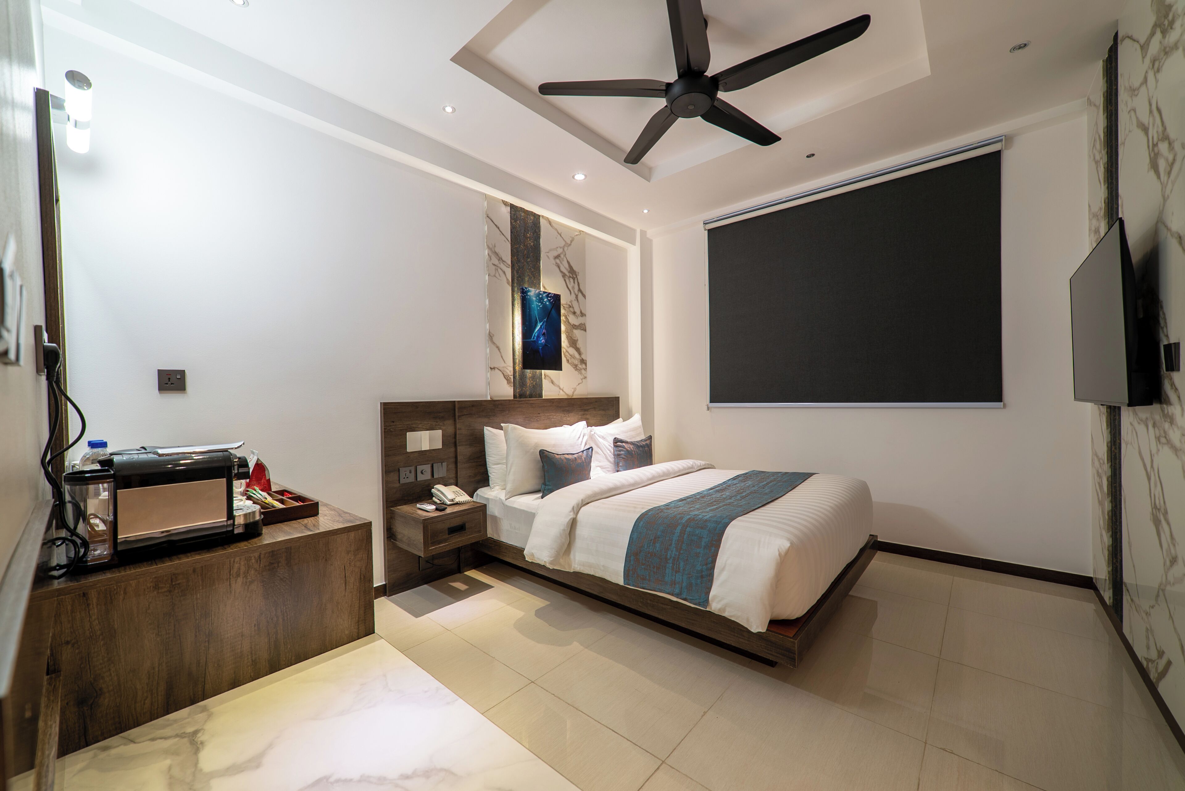 A modern bedroom with a bed, nightstand, desk, ceiling fan, and a large window.