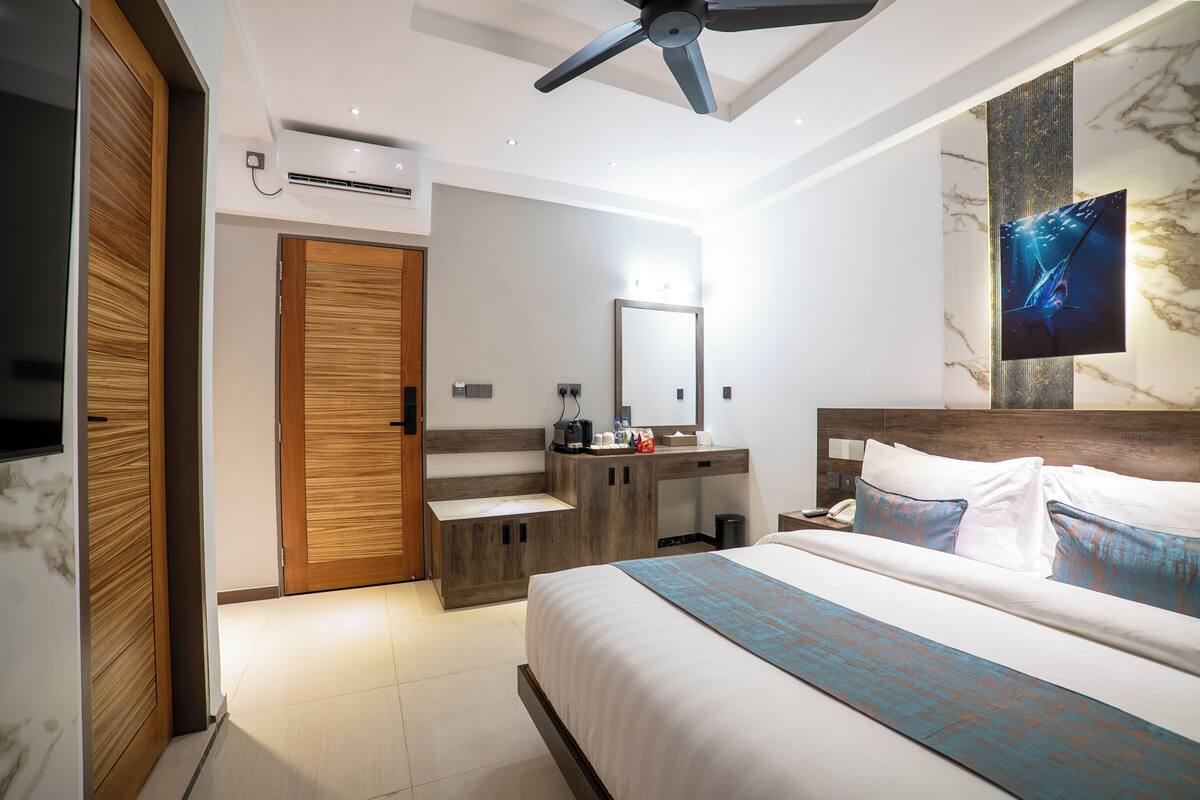 A modern hotel room with a bed, a vanity, a mirror, and a ceiling fan.