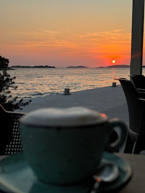 Une vue sur le coucher de soleil depuis une terrasse, avec une tasse posée sur une soucoupe.