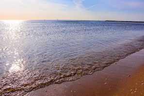 A beach with calm water, a sandy shore, and a distant pier. - Cala Del Porto 2-room-apartment 3P (Marettimo)